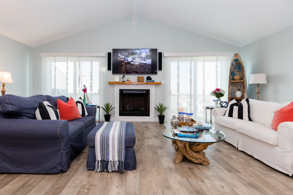フィラデルフィアにあるラグジュアリーな広いビーチスタイルのおしゃれなリビング (青い壁、ラミネートの床、標準型暖炉、木材の暖炉まわり、壁掛け型テレビ、茶色い床) の写真