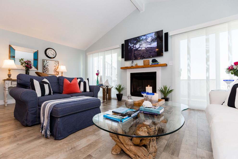 Источник вдохновения для домашнего уюта: большая парадная, открытая гостиная комната в морском стиле с синими стенами, полом из ламината, стандартным камином, фасадом камина из дерева, телевизором на стене и бежевым полом