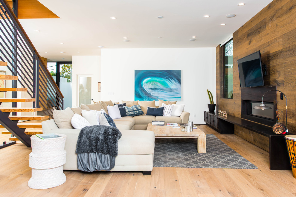 Offenes Modernes Wohnzimmer mit weißer Wandfarbe, braunem Holzboden, Gaskamin, Kaminumrandung aus Holz, TV-Wand, braunem Boden und Holzwänden in Los Angeles
