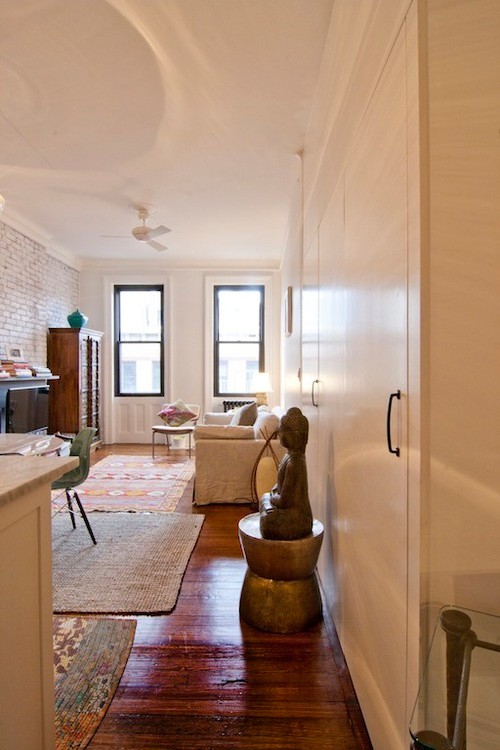 Kleines, Offenes Eklektisches Wohnzimmer mit dunklem Holzboden, weißer Wandfarbe, Kamin, Kaminumrandung aus Stein, freistehendem TV und braunem Boden in New York