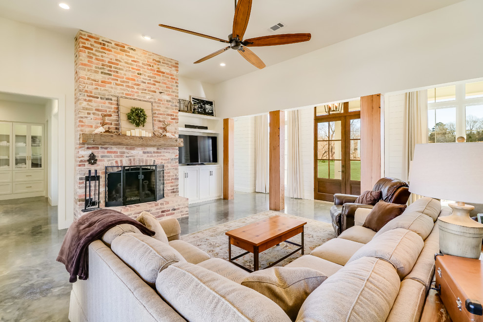 Photo of a large farmhouse open plan living room in Jackson with white walls, concrete flooring, a standard fireplace, a brick fireplace surround, a built-in media unit and grey floors.