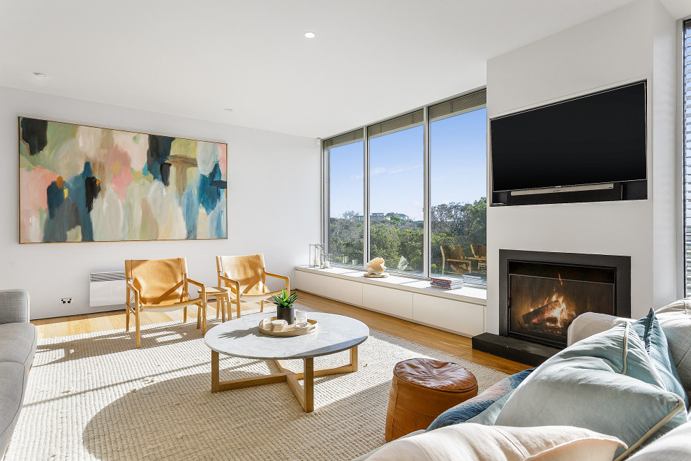 Example of a trendy open concept medium tone wood floor and brown floor living room design in Melbourne with white walls, a standard fireplace and a wall-mounted tv