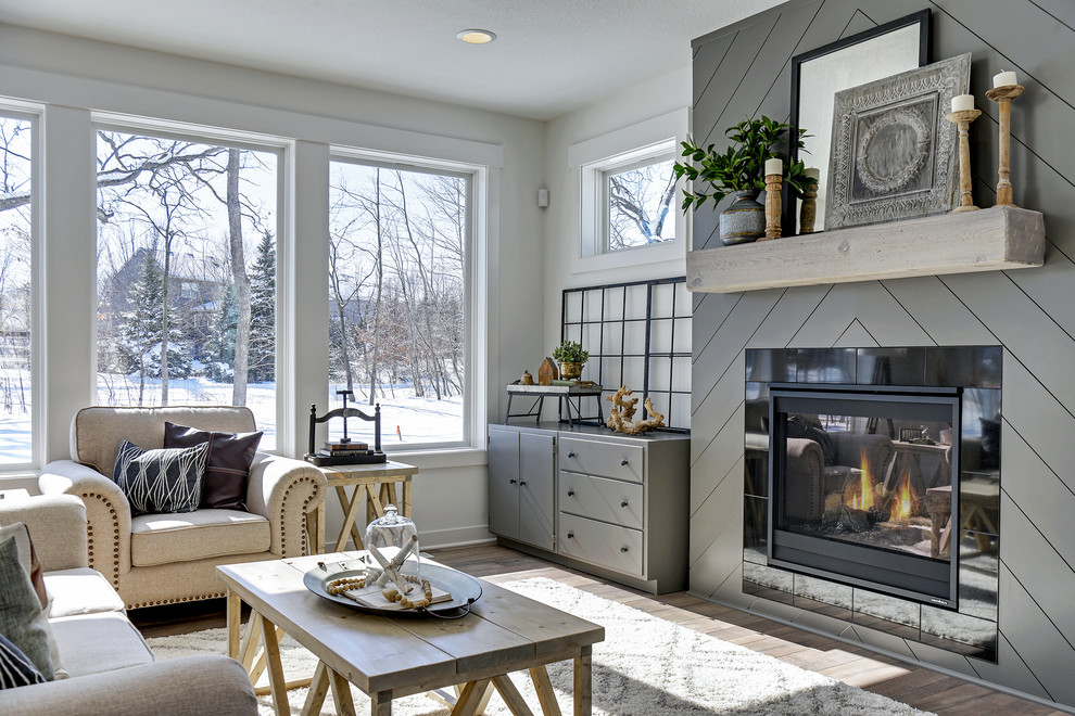 This is an example of a medium sized rural open plan living room in Minneapolis with white walls, laminate floors, a standard fireplace, a tiled fireplace surround, no tv and brown floors.