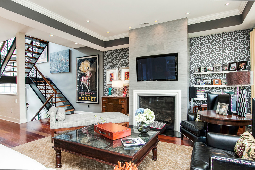 Cette image montre un grand salon design ouvert avec un mur gris, un sol en bois brun, une cheminée standard, un téléviseur encastré et un escalier.
