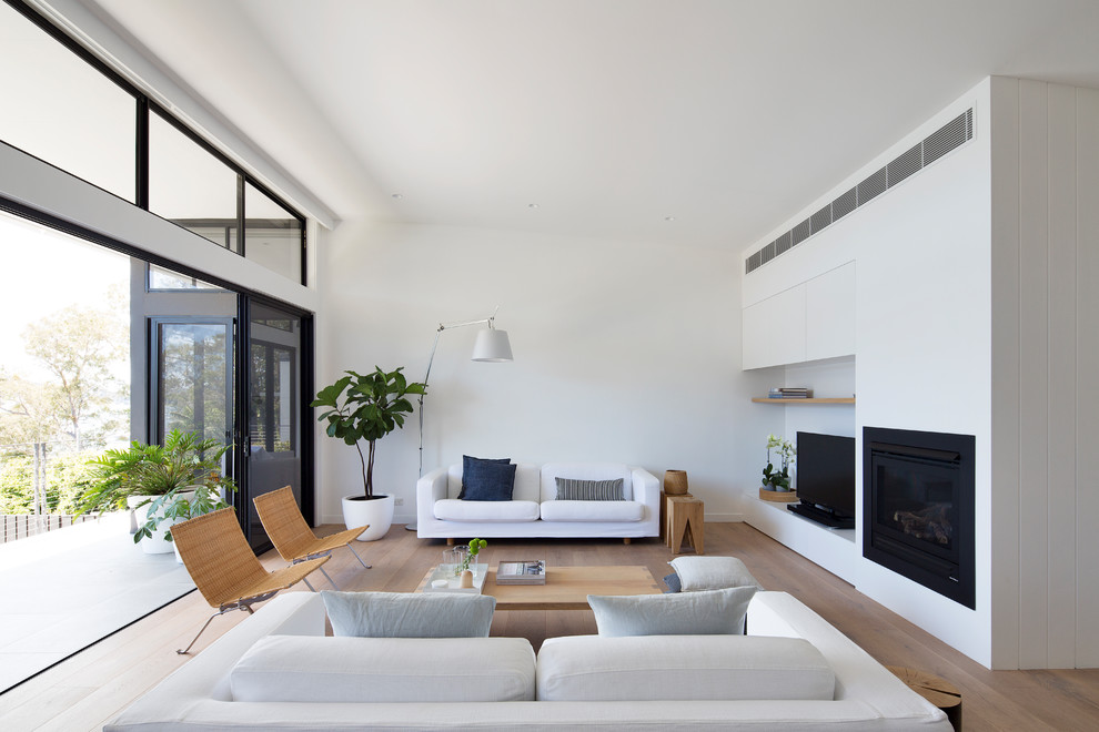 Ejemplo de salón contemporáneo con paredes blancas, suelo de madera en tonos medios, todas las chimeneas, televisor independiente y suelo marrón