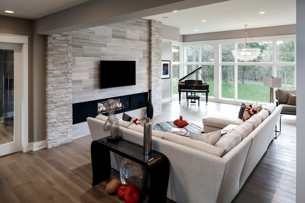 Foto de salón para visitas clásico renovado grande con paredes grises, suelo de madera clara, chimenea lineal, marco de chimenea de piedra y televisor colgado en la pared