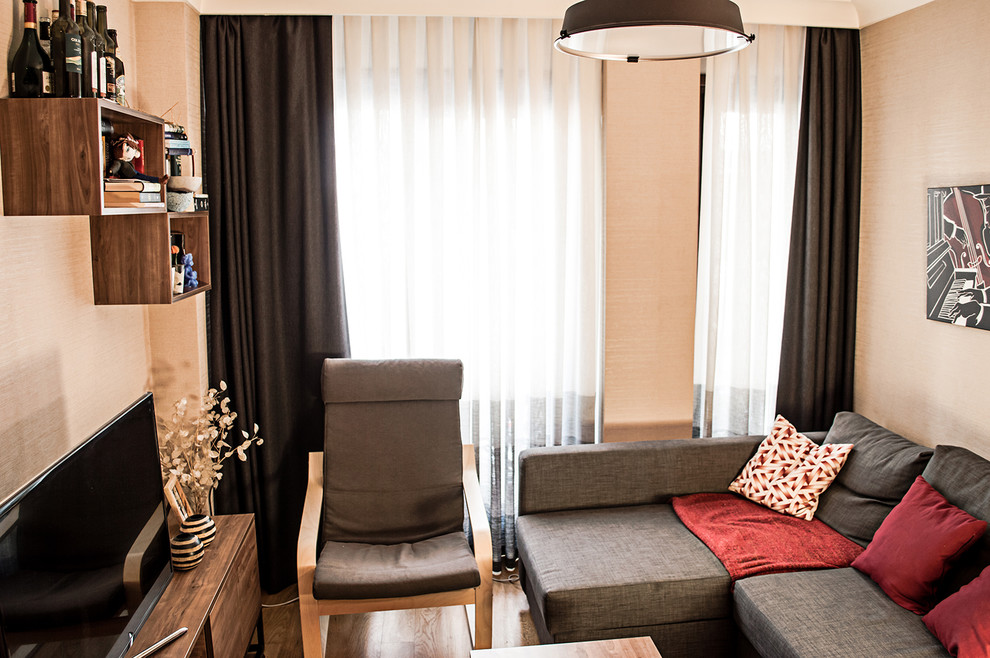 Стильный дизайн: маленькая открытая гостиная комната в стиле модернизм с бежевыми стенами, полом из ламината, отдельно стоящим телевизором и коричневым полом без камина для на участке и в саду - последний тренд