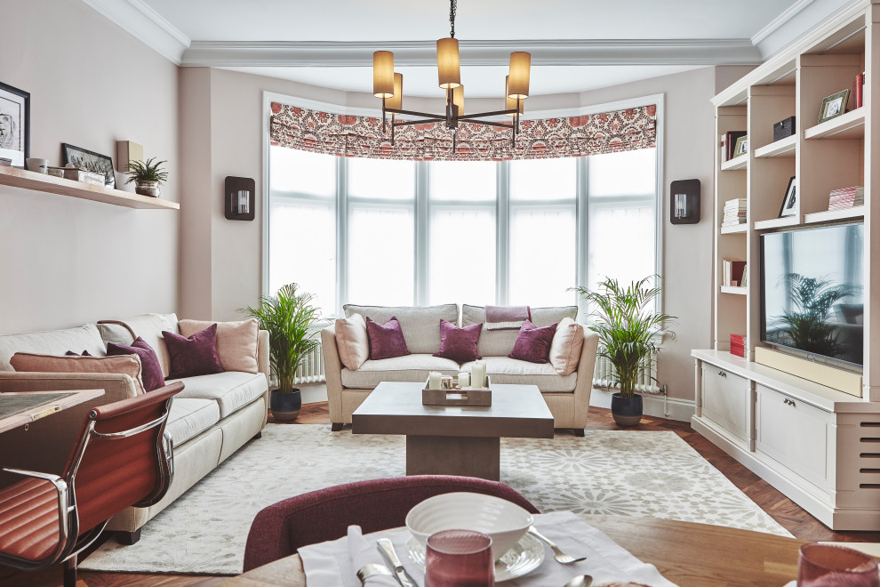 На фото: большая открытая гостиная комната в стиле неоклассика (современная классика) с паркетным полом среднего тона, отдельно стоящим телевизором, коричневым полом и розовыми стенами