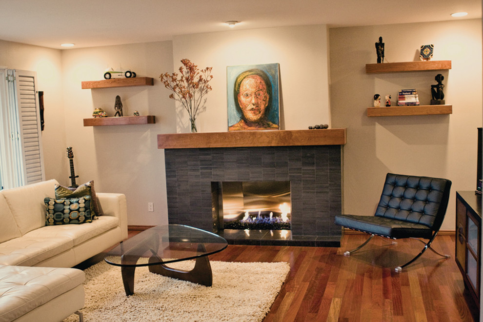 Immagine di un grande soggiorno minimalista chiuso con pareti beige, pavimento in legno massello medio, camino classico e cornice del camino piastrellata