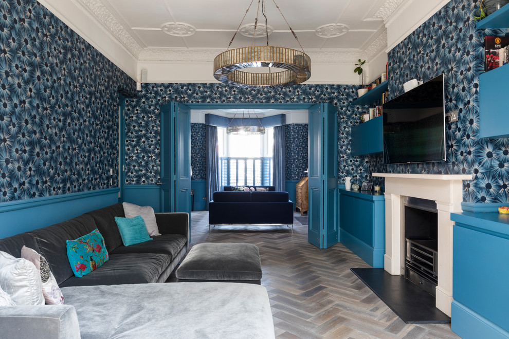Свежая идея для дизайна: открытая гостиная комната среднего размера в современном стиле с синими стенами, темным паркетным полом, стандартным камином, фасадом камина из камня, телевизором на стене, коричневым полом и обоями за телевизором - отличное фото интерьера