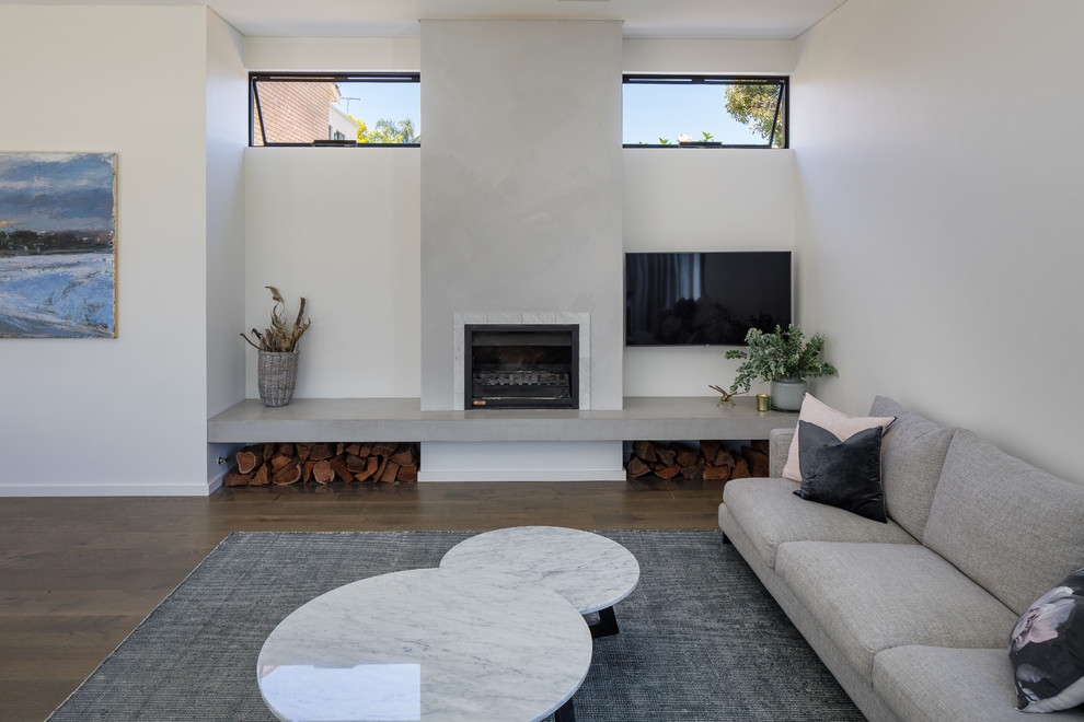 Cette image montre un grand salon design ouvert avec un mur blanc, parquet foncé, une cheminée standard, un manteau de cheminée en plâtre, un téléviseur fixé au mur et un sol marron.