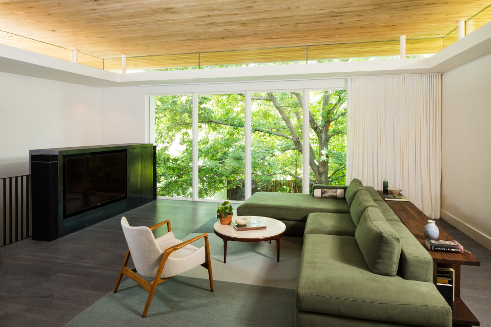 Modelo de salón abierto moderno de tamaño medio con paredes blancas, suelo de madera oscura y televisor retractable