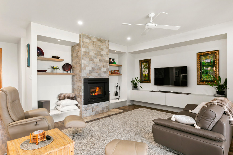 Modern inredning av ett vardagsrum, med vita väggar, mellanmörkt trägolv, en standard öppen spis, en spiselkrans i sten, en väggmonterad TV och brunt golv