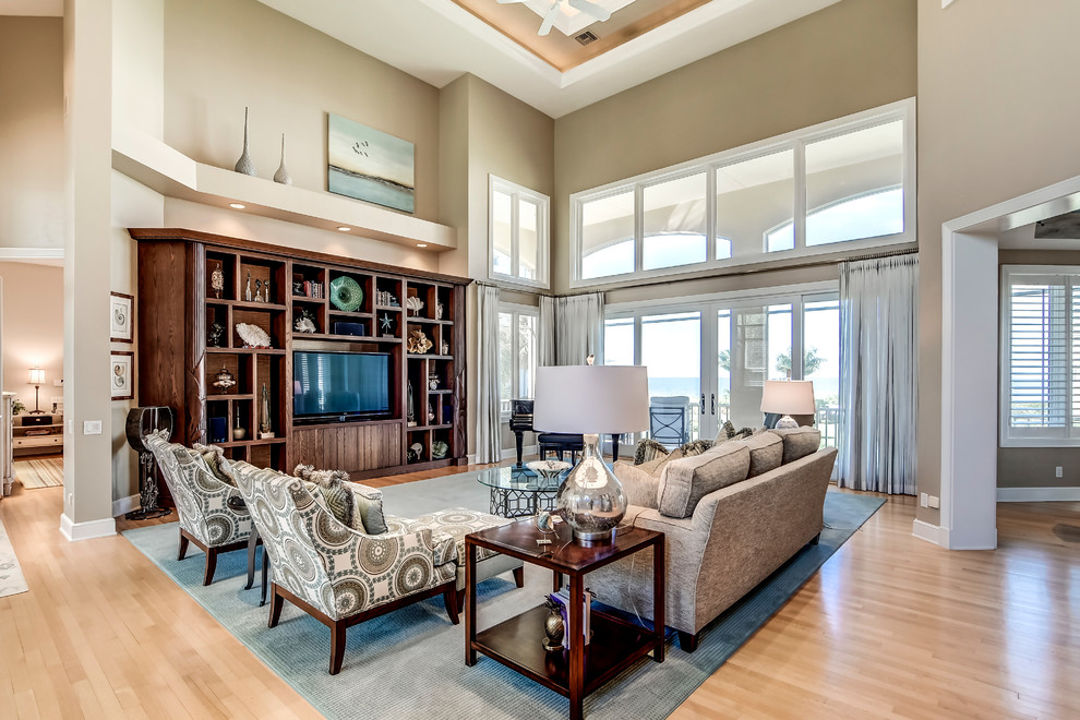 Example of a large beach style open concept medium tone wood floor living room design in Miami with beige walls and a media wall