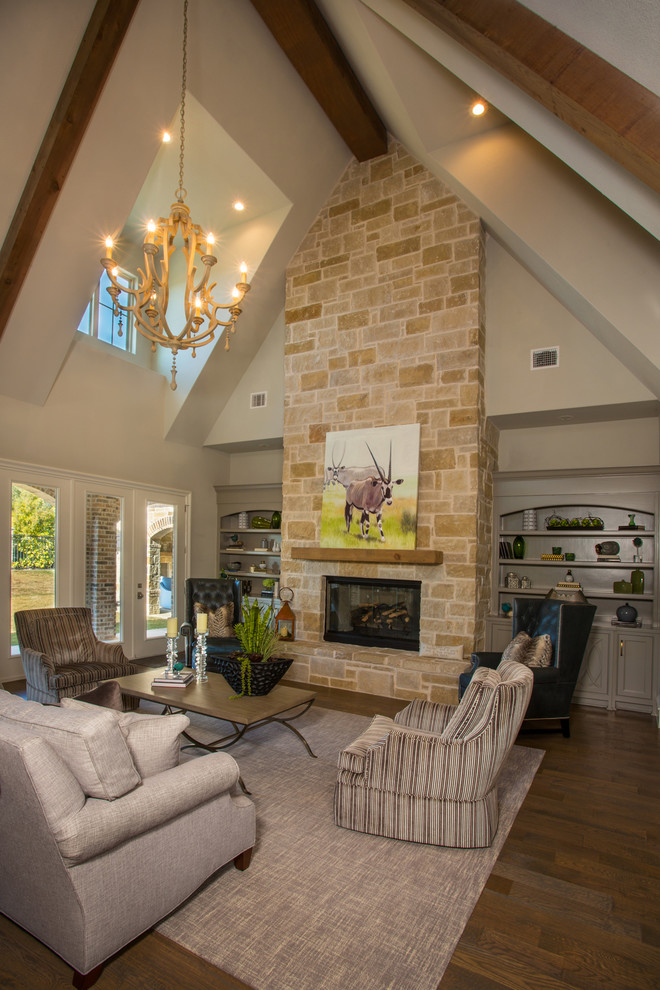 Exemple d'un grand salon chic ouvert avec un mur blanc, un sol en bois brun, une cheminée standard, un manteau de cheminée en pierre et un sol marron.