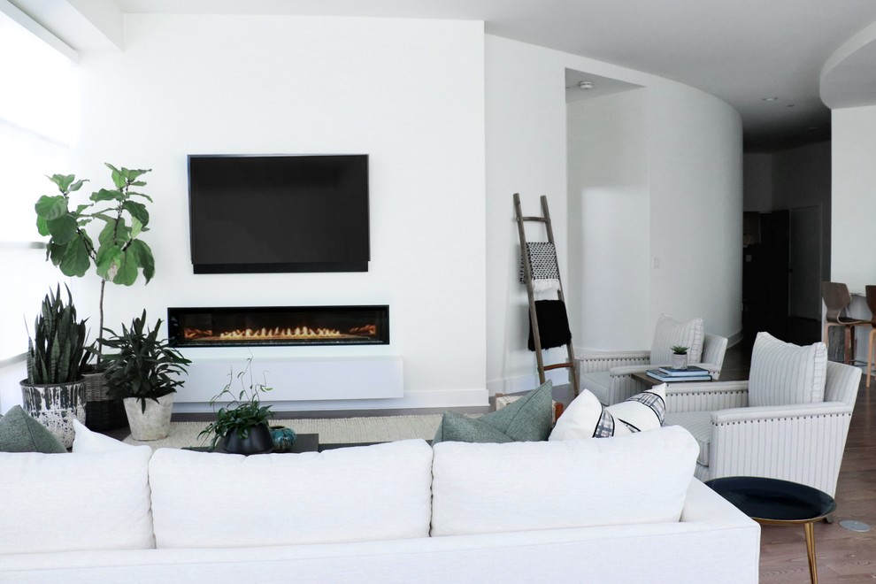 Immagine di un ampio soggiorno minimal stile loft con pareti bianche, pavimento in legno massello medio, camino sospeso, cornice del camino in pietra, TV a parete e pavimento marrone