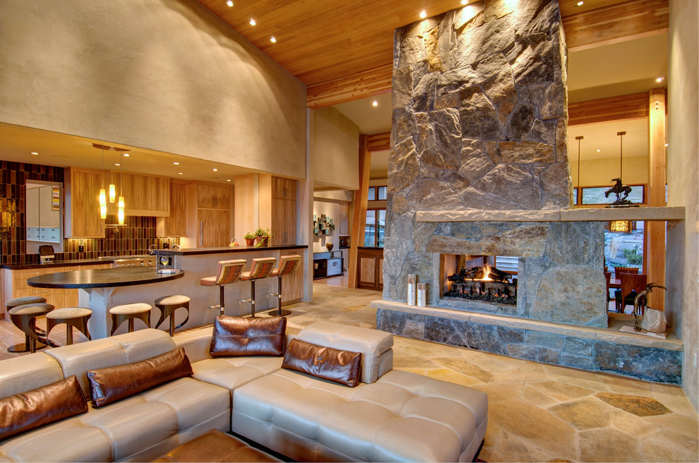 Cette image montre un salon design ouvert avec une cheminée double-face et un manteau de cheminée en pierre.