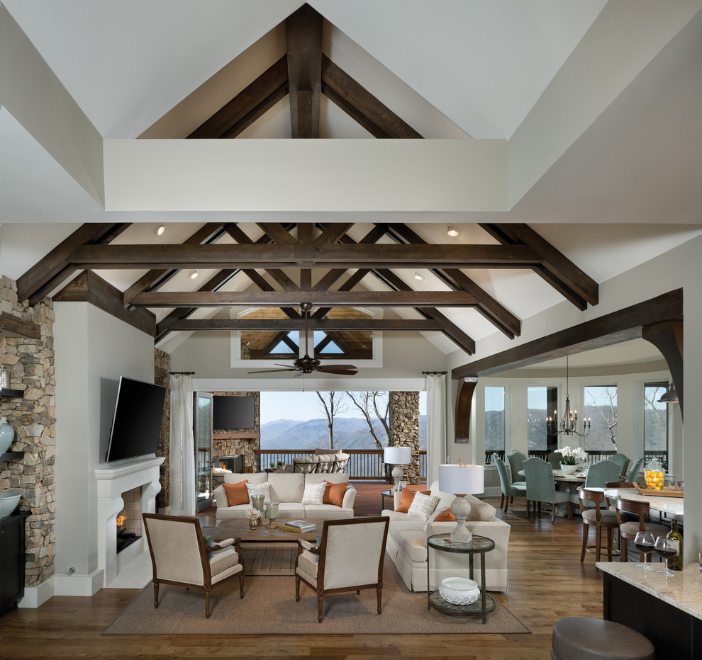 Cette image montre un grand salon traditionnel ouvert avec un mur gris, un sol en bois brun, une cheminée standard, un téléviseur fixé au mur, une salle de réception et un sol marron.