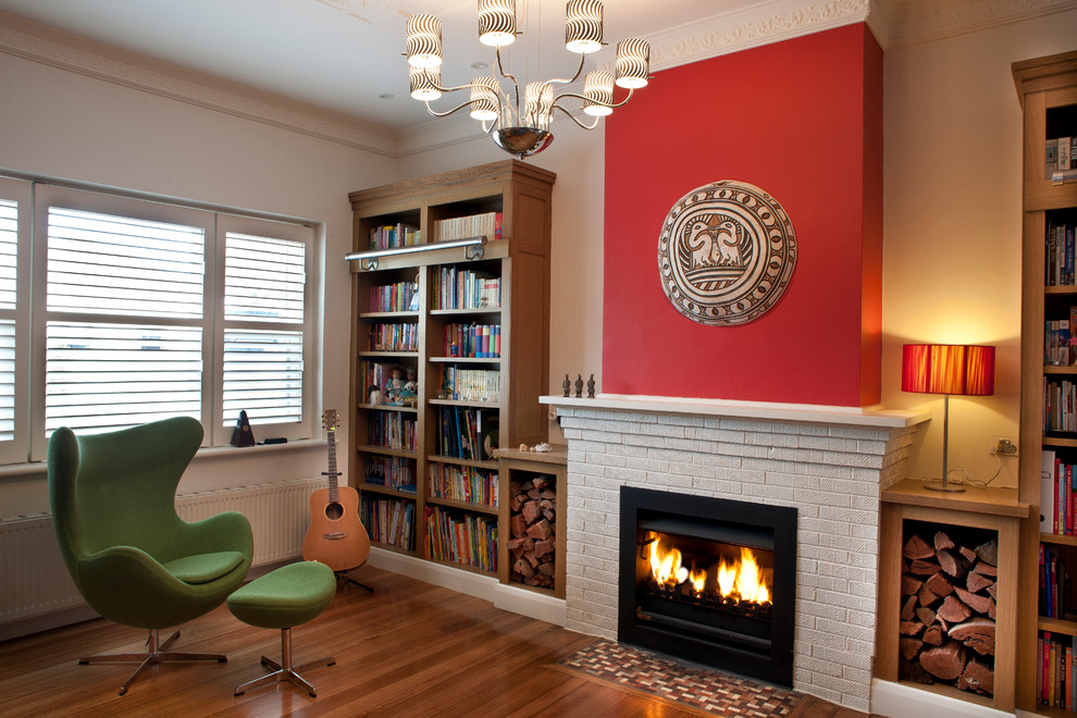 Imagen de biblioteca en casa cerrada tradicional renovada sin televisor con paredes rojas, suelo de madera en tonos medios, todas las chimeneas y marco de chimenea de ladrillo