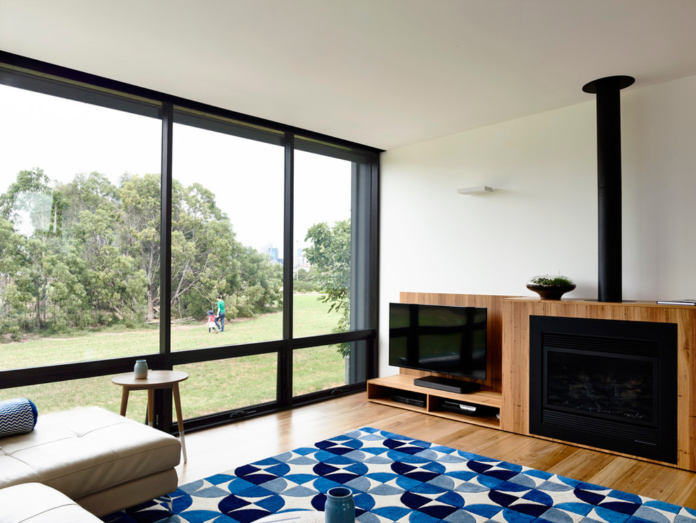 Modelo de salón abierto contemporáneo pequeño con suelo de madera clara, pared multimedia y estufa de leña