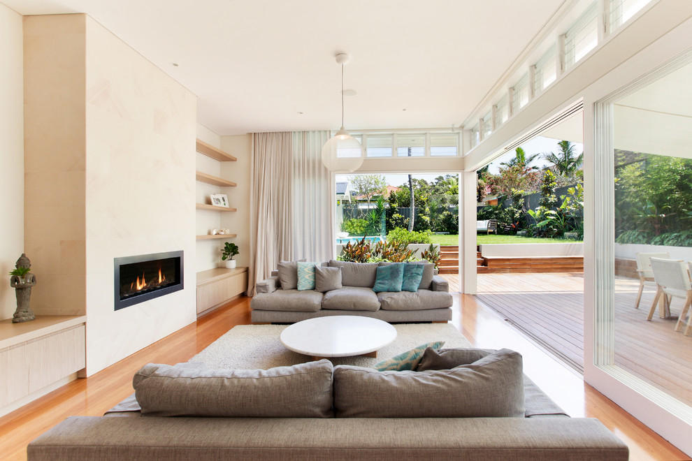 Mittelgroßes, Offenes Maritimes Wohnzimmer mit weißer Wandfarbe, hellem Holzboden, Kamin, Kaminumrandung aus Stein und TV-Wand in Sydney