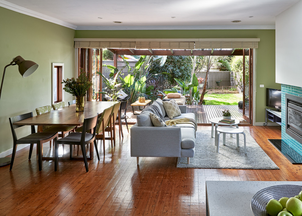 Großes, Offenes Modernes Wohnzimmer mit grüner Wandfarbe, braunem Holzboden, Kamin, gefliester Kaminumrandung, verstecktem TV und braunem Boden in Melbourne