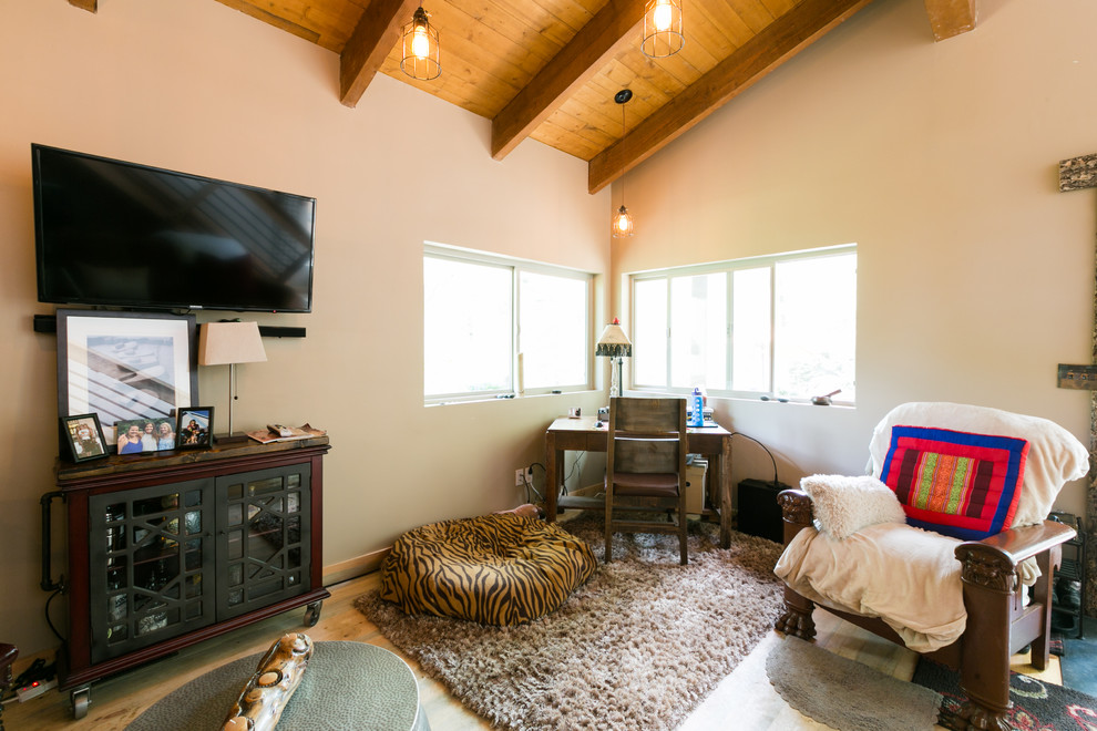Diseño de salón tipo loft rural pequeño con paredes beige, suelo de madera en tonos medios, estufa de leña, marco de chimenea de metal y televisor colgado en la pared