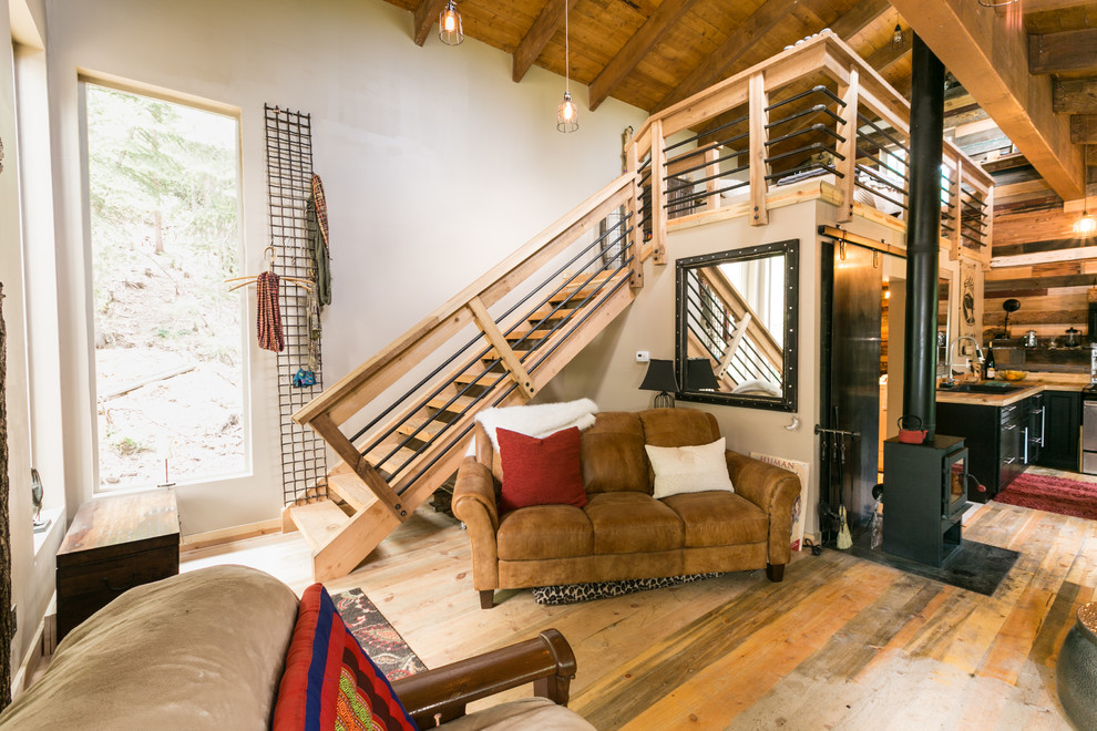 Immagine di un piccolo soggiorno rustico stile loft con pareti beige, pavimento in legno massello medio, stufa a legna, cornice del camino in metallo e TV a parete