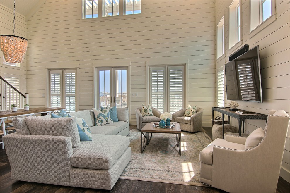 На фото: большая открытая гостиная комната в морском стиле с белыми стенами, паркетным полом среднего тона, телевизором на стене и коричневым полом с