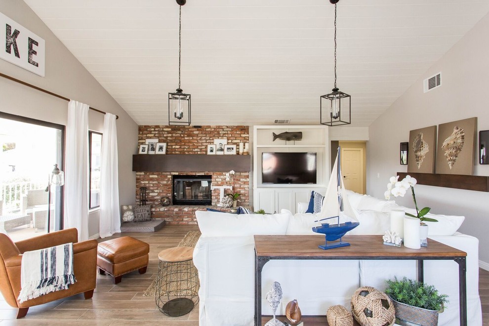 This is an example of a medium sized beach style mezzanine living room in Los Angeles with beige walls, medium hardwood flooring, a standard fireplace, a brick fireplace surround, a wall mounted tv and brown floors.