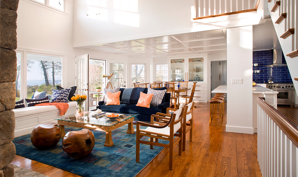 На фото: открытая гостиная комната в морском стиле с белыми стенами, паркетным полом среднего тона, коричневым полом и синим диваном