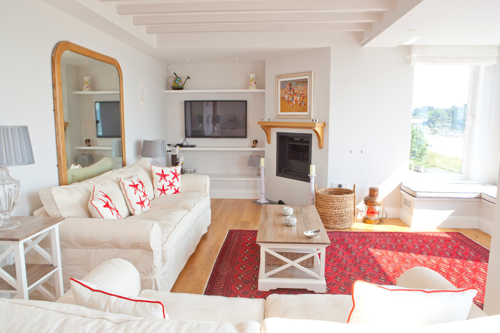 Immagine di un soggiorno stile marinaro chiuso con pareti bianche, parquet chiaro, camino ad angolo e TV a parete