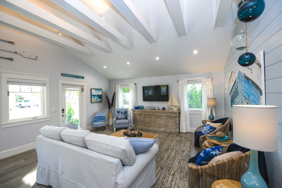 タンパにある高級なビーチスタイルのおしゃれなLDK (青い壁、磁器タイルの床、壁掛け型テレビ、グレーの床) の写真