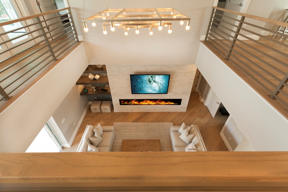 Стильный дизайн: большая парадная, двухуровневая гостиная комната в современном стиле с серыми стенами, светлым паркетным полом, горизонтальным камином, фасадом камина из каменной кладки, телевизором на стене и коричневым полом - последний тренд