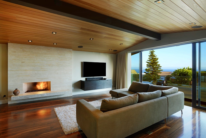 Diseño de salón tipo loft actual de tamaño medio con paredes beige, suelo de madera oscura, chimenea lineal, marco de chimenea de piedra y televisor independiente