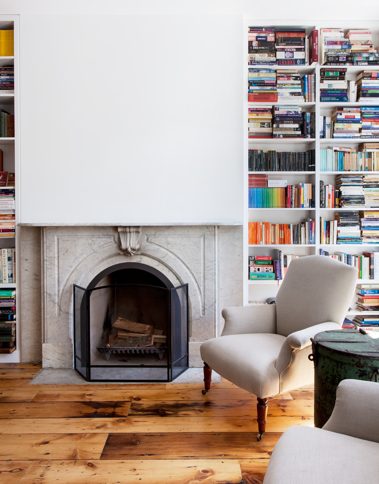 Cette image montre un salon design de taille moyenne et ouvert avec une bibliothèque ou un coin lecture, un mur blanc, un sol en bois brun, une cheminée standard, un manteau de cheminée en pierre et un sol marron.