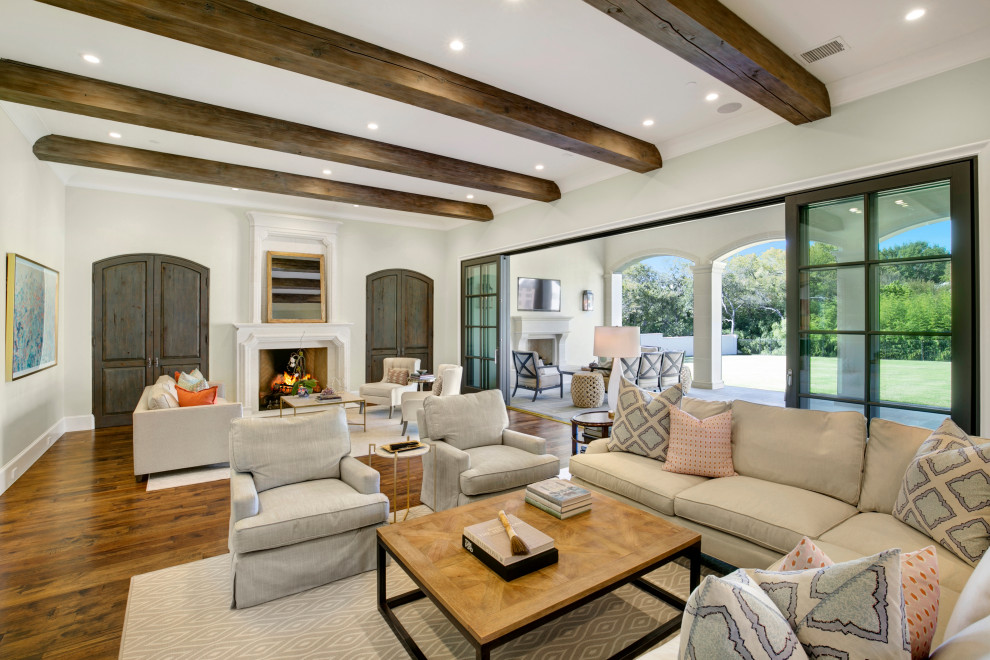 Design ideas for a large open plan living room in Dallas with white walls, medium hardwood flooring, a standard fireplace, a stone fireplace surround, a built-in media unit, brown floors and exposed beams.