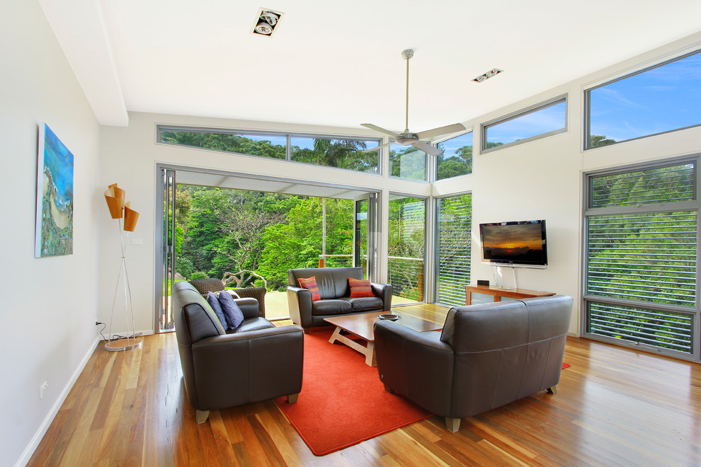 Imagen de salón abierto minimalista de tamaño medio con paredes blancas, suelo de madera en tonos medios y televisor colgado en la pared