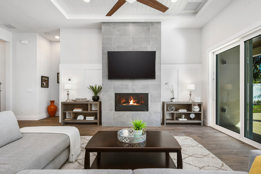 Идея дизайна: большая открытая гостиная комната в стиле модернизм с серыми стенами, полом из керамогранита, стандартным камином, фасадом камина из плитки, телевизором на стене, коричневым полом и ковром на полу