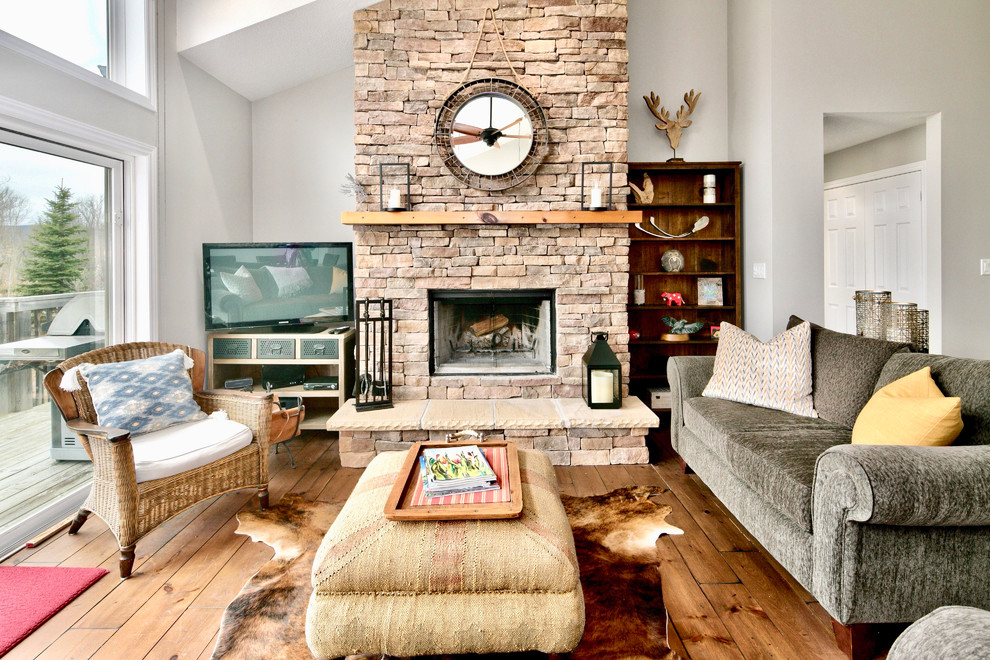 Example of a mountain style open concept medium tone wood floor and brown floor living room design in Toronto with white walls, a standard fireplace, a stone fireplace and a tv stand