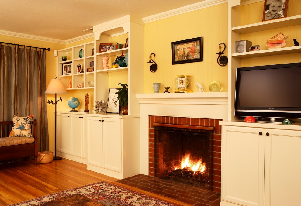 Réalisation d'un grand salon tradition ouvert avec un mur jaune, un sol en bois brun, une cheminée standard, un manteau de cheminée en brique et un téléviseur indépendant.