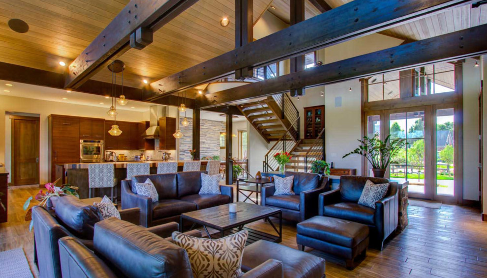 This is an example of a large rustic open plan living room in Denver with beige walls, light hardwood flooring, no fireplace, a stone fireplace surround, a wall mounted tv and brown floors.