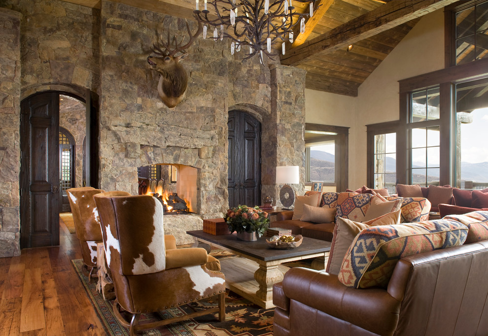 Rustikales Wohnzimmer mit beiger Wandfarbe, dunklem Holzboden, Tunnelkamin, Kaminumrandung aus Stein und Steinwänden in Denver