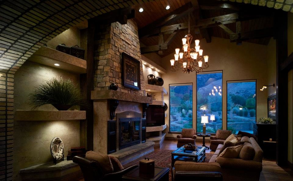 Cette photo montre un grand salon chic ouvert avec une salle de réception, un mur beige, un sol en bois brun, une cheminée standard, un manteau de cheminée en pierre et un téléviseur indépendant.