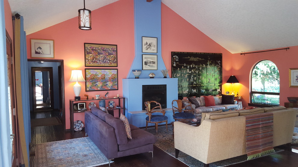 На фото: большая открытая гостиная комната в стиле фьюжн с разноцветными стенами, темным паркетным полом, стандартным камином и фасадом камина из штукатурки