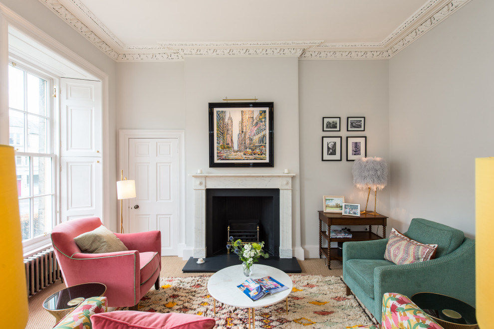 На фото: гостиная комната в стиле неоклассика (современная классика) с серыми стенами, ковровым покрытием, стандартным камином, бежевым полом и эркером