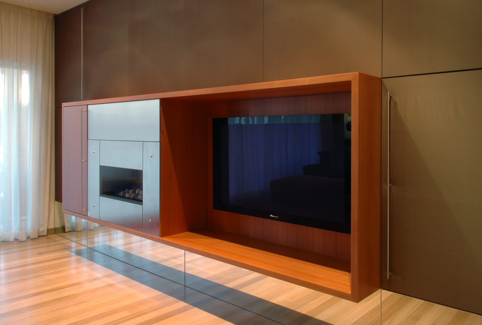 Modelo de salón abierto actual de tamaño medio con suelo de madera clara, chimeneas suspendidas, marco de chimenea de metal y pared multimedia