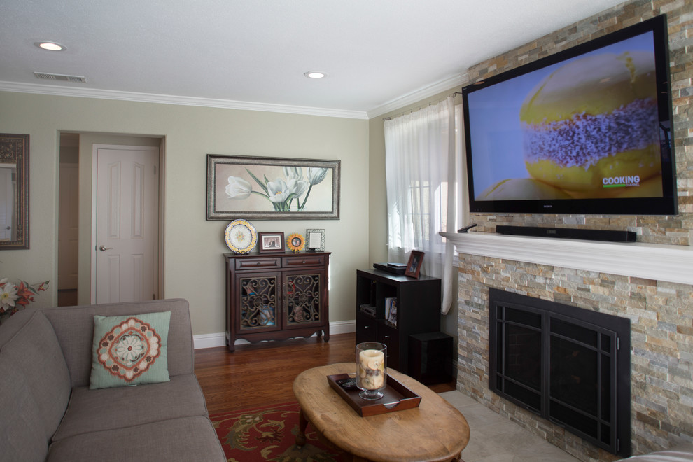 Imagen de salón cerrado clásico de tamaño medio con paredes beige, suelo de madera en tonos medios, marco de chimenea de piedra, televisor colgado en la pared y estufa de leña