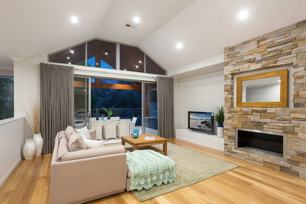 Offenes Maritimes Wohnzimmer mit weißer Wandfarbe, braunem Holzboden, Kamin, Kaminumrandung aus Stein, freistehendem TV und beigem Boden in Perth