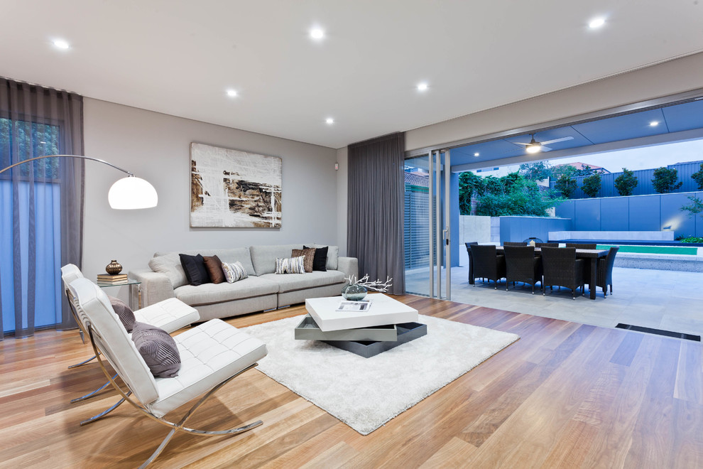 Diseño de salón abierto actual sin chimenea con paredes grises, suelo de madera clara, suelo beige y alfombra